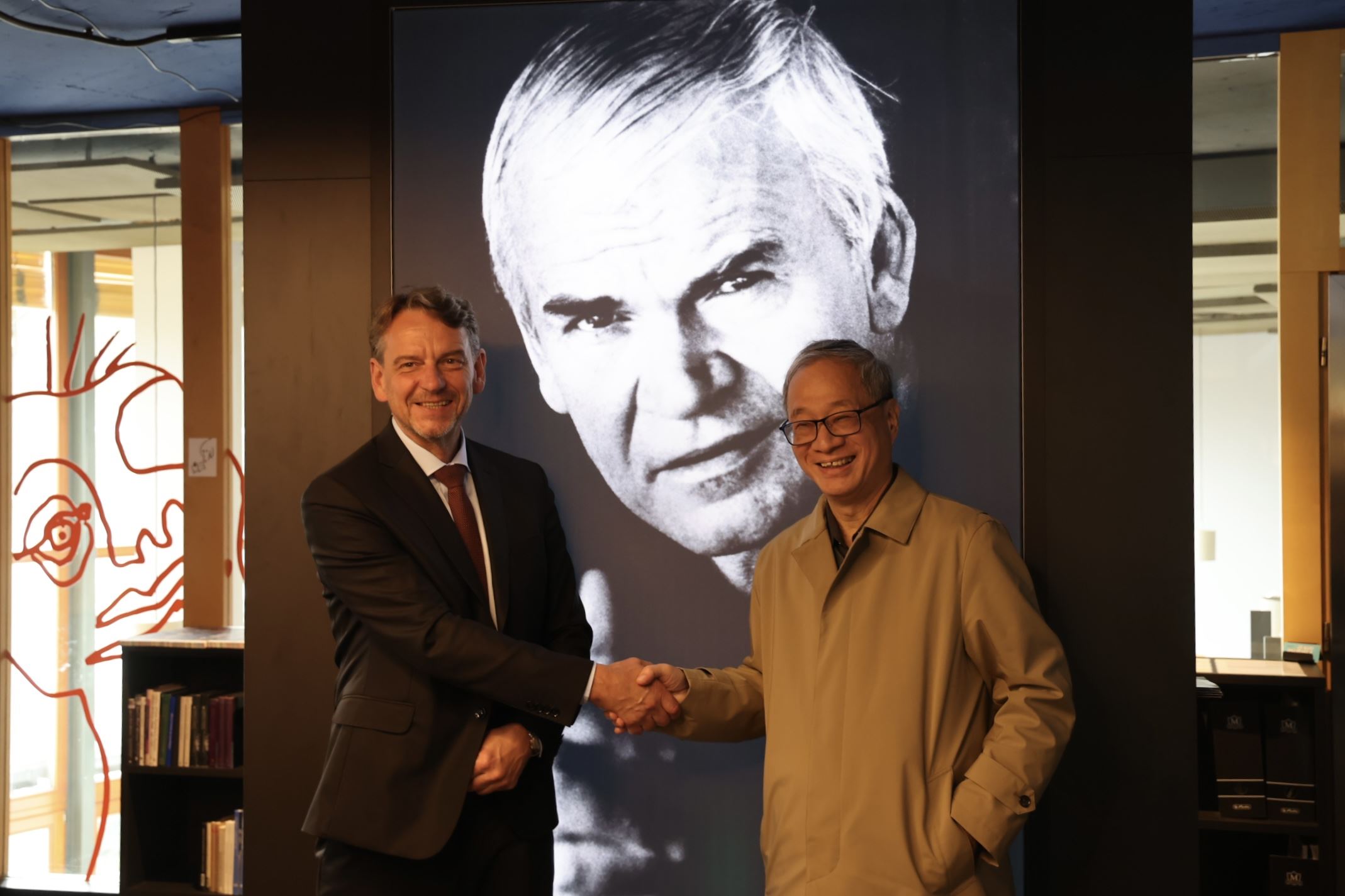モラヴィア図書館のTomáš Kubíček館長（左）と李遠部長（右）。『存在の耐えられない軽さ』で知られるチェコスロバキア出身の作家ミラン・クンデラ氏の写真の前で。（文化部）