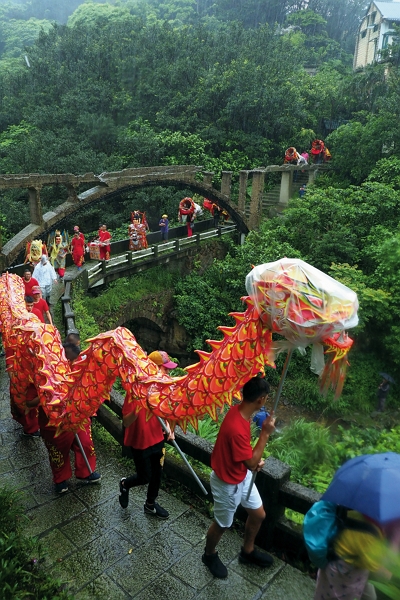 媽祖陣頭穿過山城陡坡小巷，踩過高低階梯，鑽過水圳橋，伴隨著春雨瀟瀟。（林格立攝）